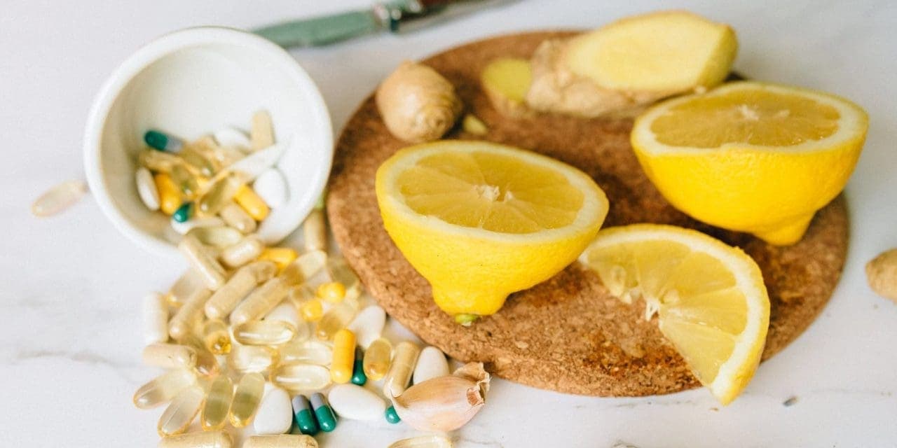 tumbled bowl with different types of capsules alongside with sliced lemons, ginger and garlic on a small cutting board