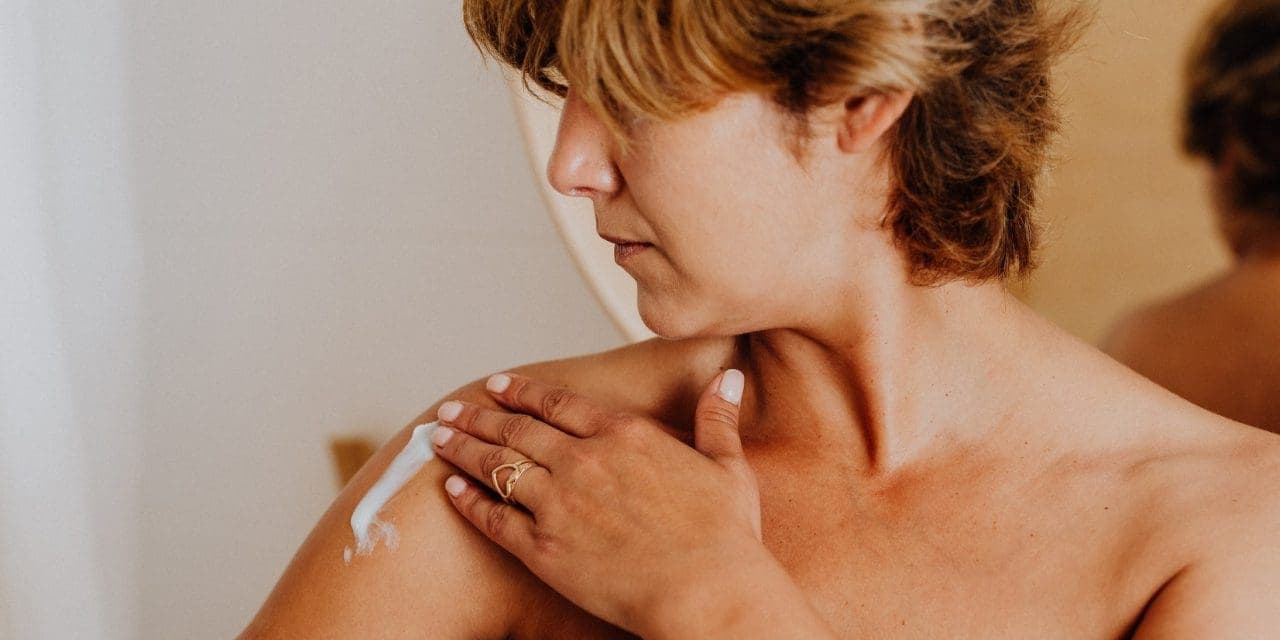 closeup of woman's naked shoulder applying some cream